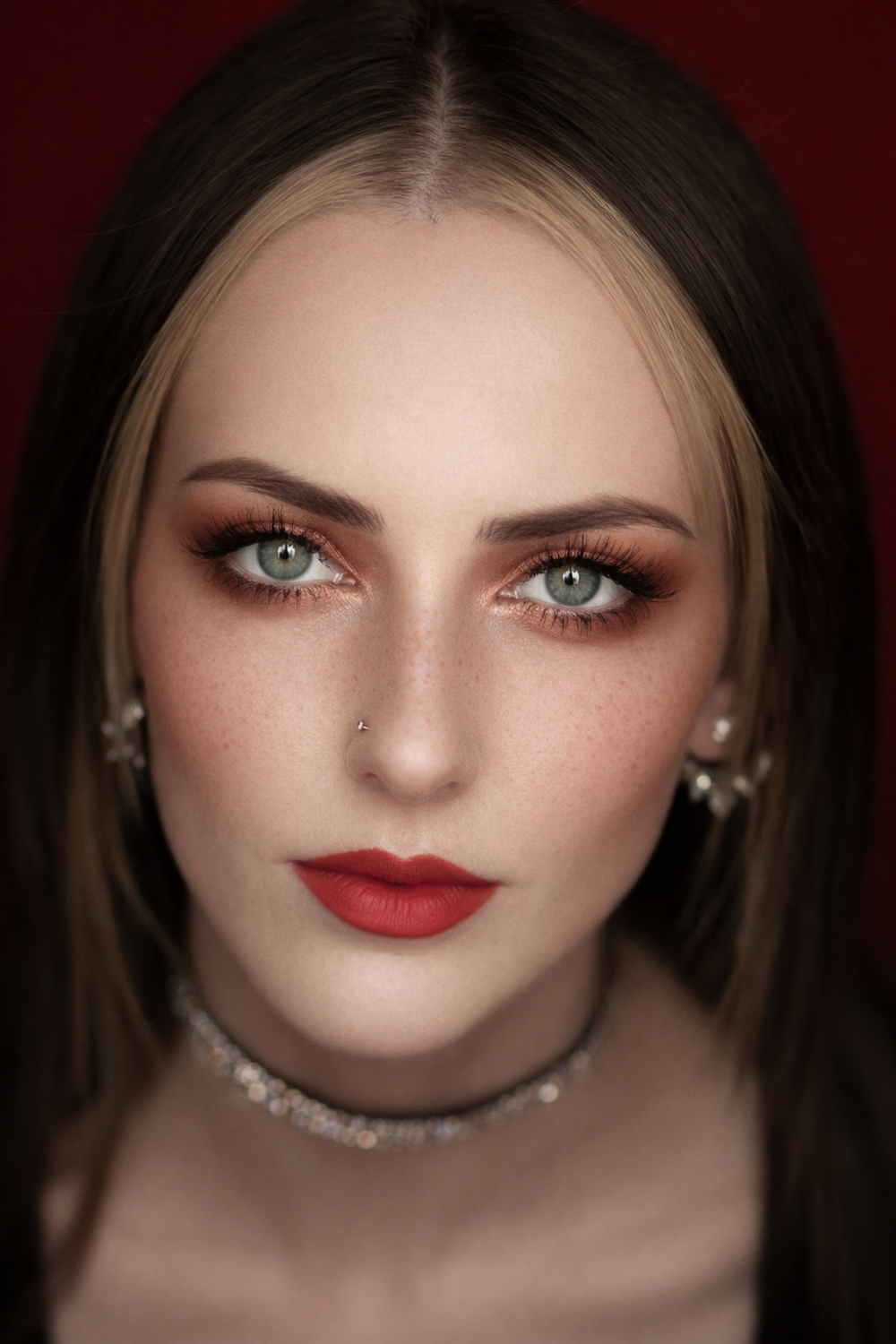 Close-up beauty portrait with dramatic lighting showcasing red lipstick, smokey eyeshadow and glowing skin.
