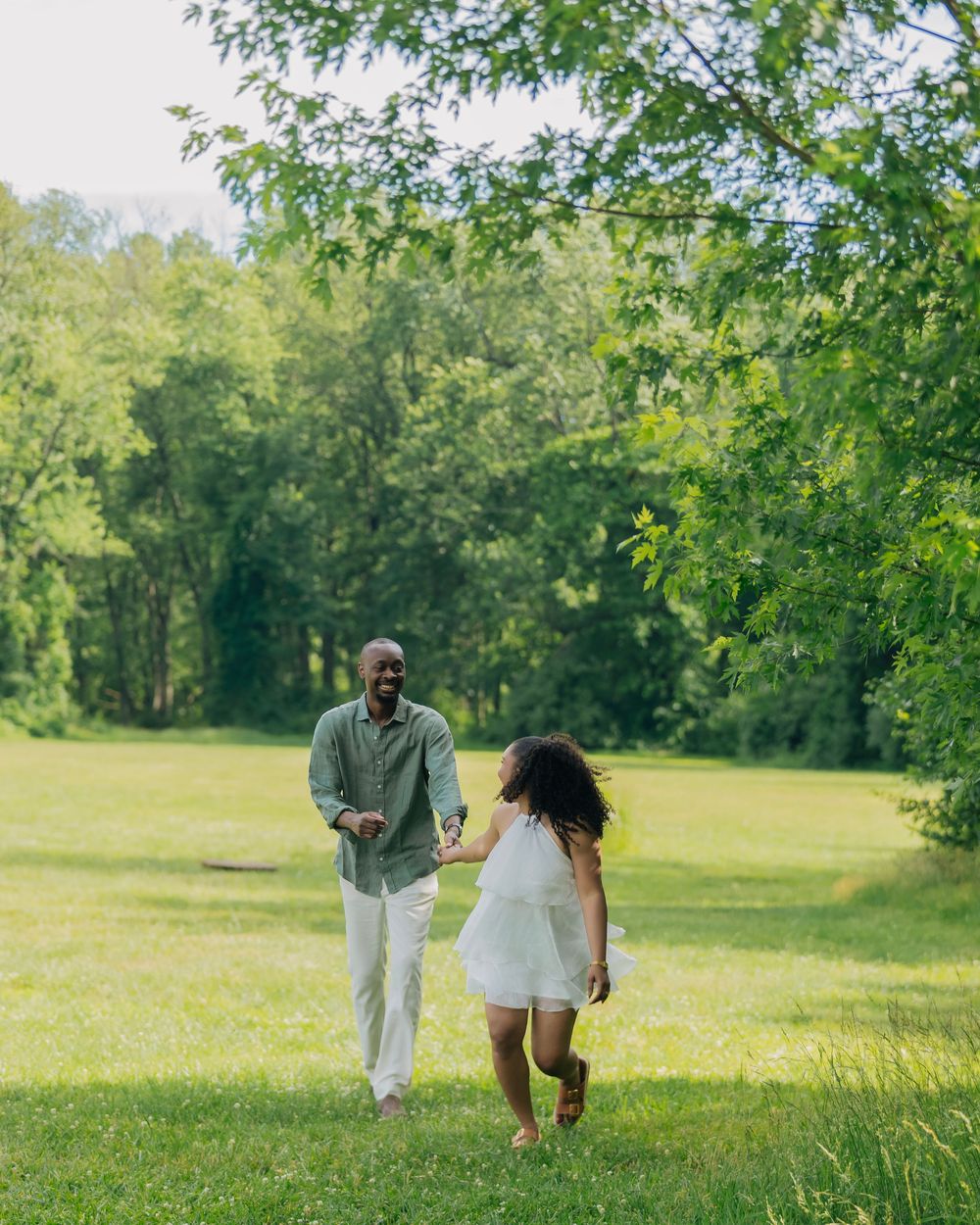 A joyful couple holds hands while walking through a lush green park on a sunny day.