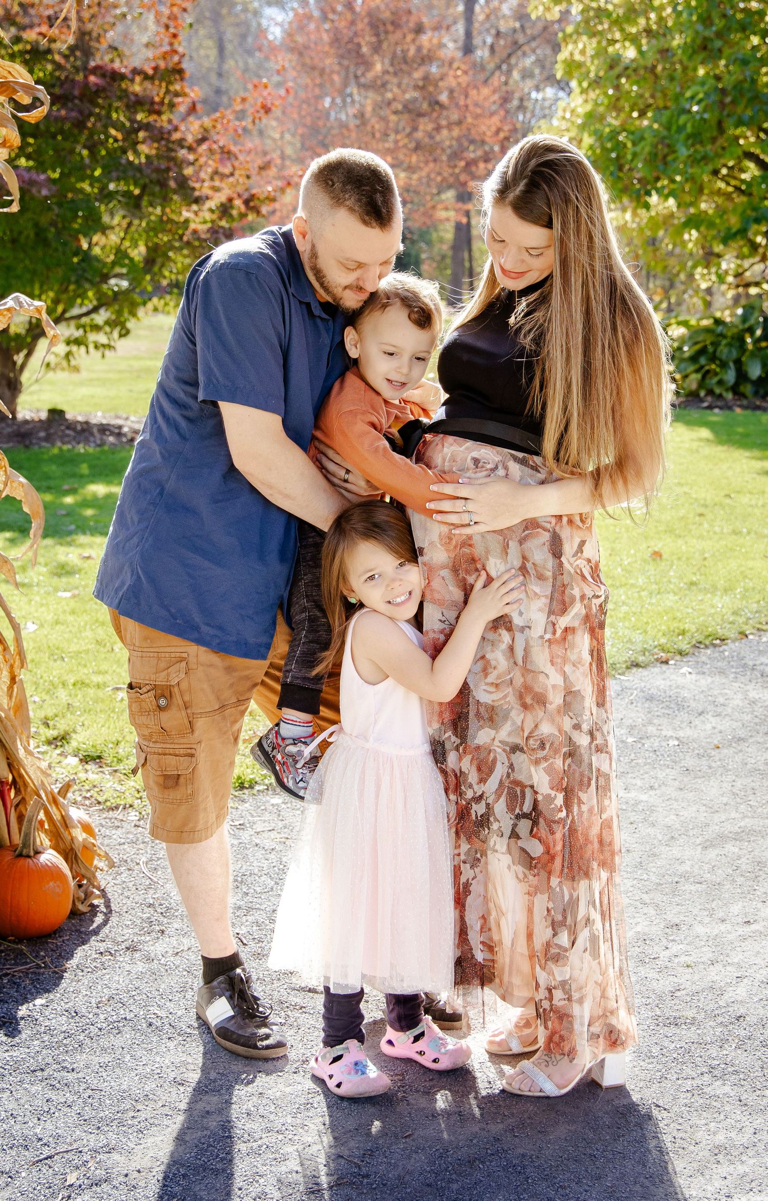 A family poses together on a path with fall foliage and a pumpkin in the background.