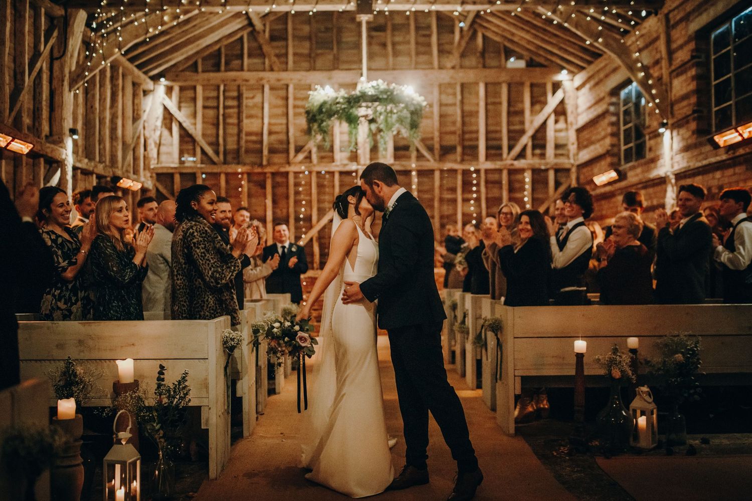 The newlyweds share their first kiss as husband and wife under Milling Barn’s elegant wooden beams, surrounded by family and friends