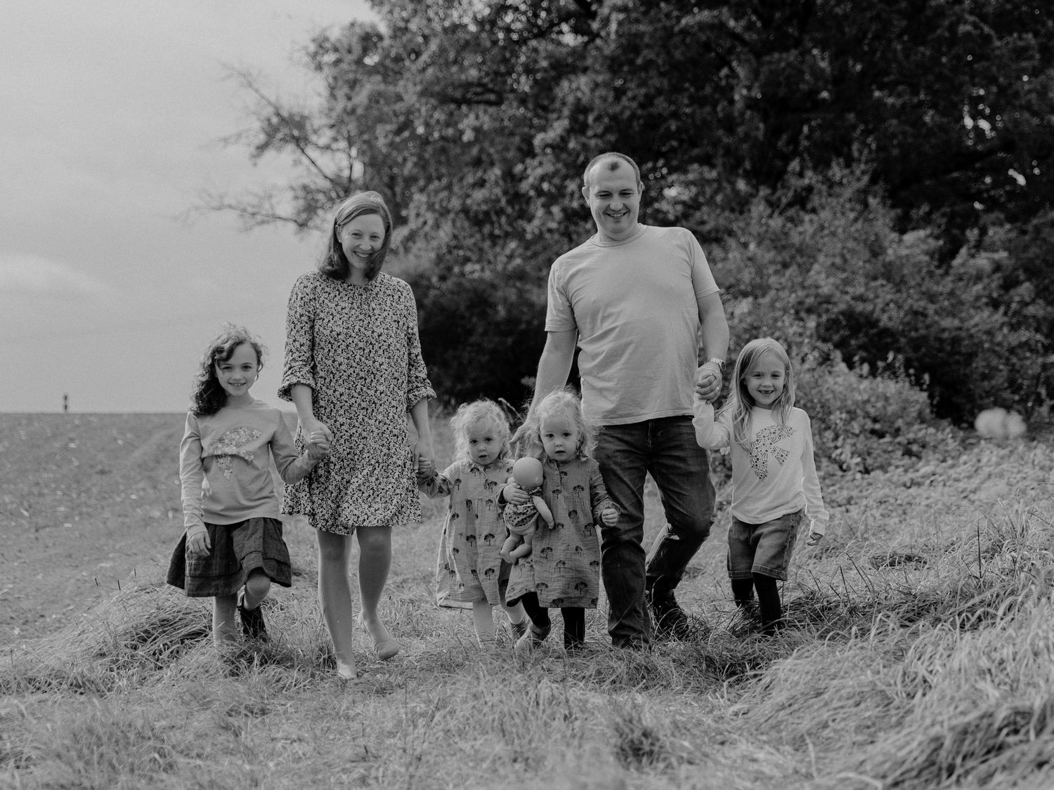 A black and white photo of a family group walking together through a grassy hillside in nature.