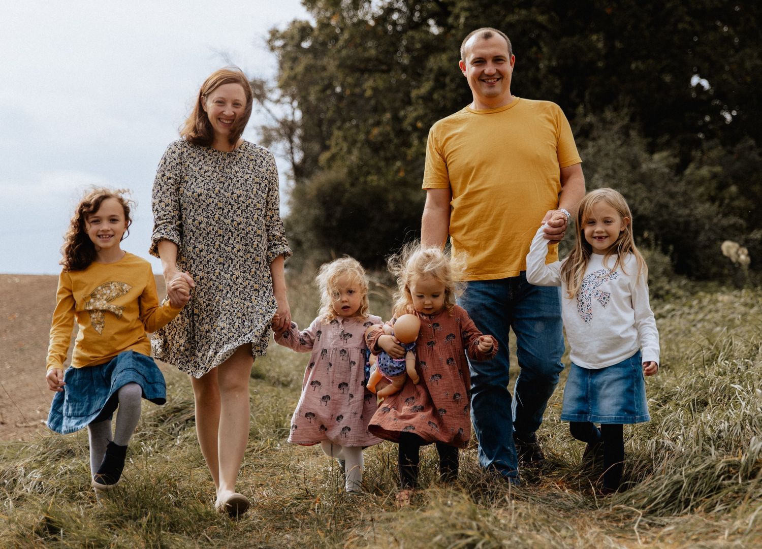 A family of six jumping and playing together on a grassy hillside during autumn.
