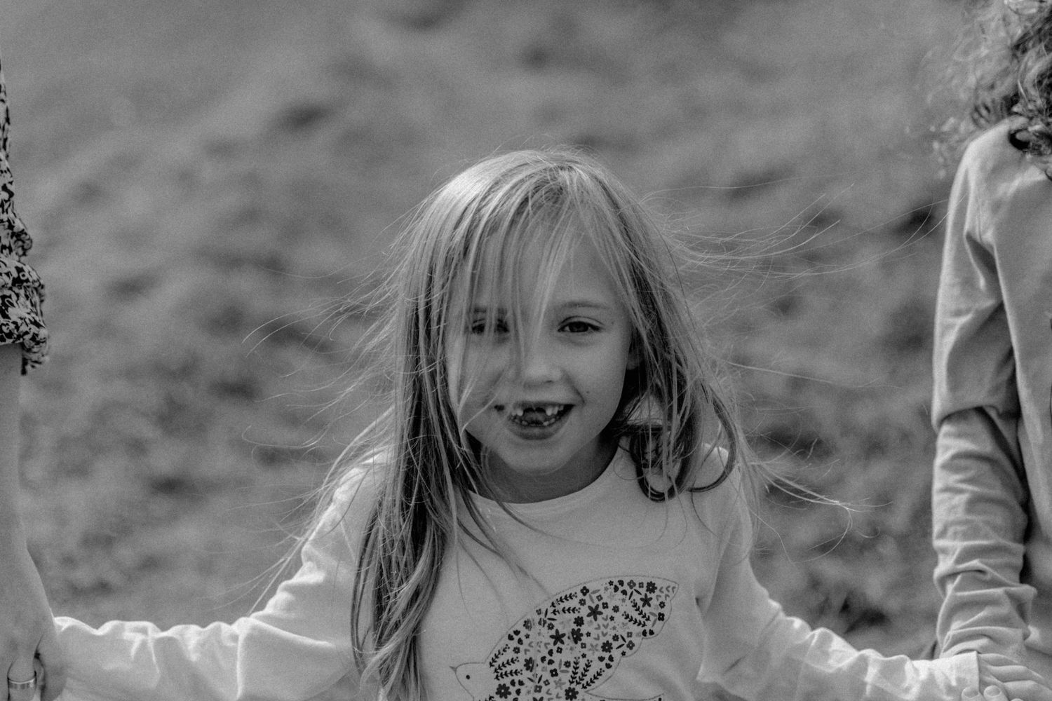 A joyful young child in a light colored shirt smiles while playing outdoors in black and white.