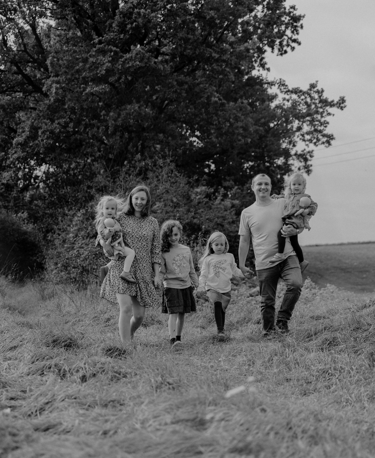 Black and white photograph of a family walking together on a hillside path surrounded by trees and tall grass.