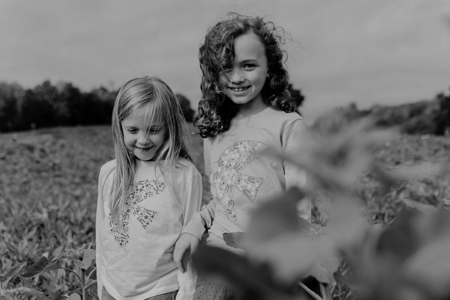 Black and white photo of two people wearing floral print shirts standing together in a field on a sunny day.