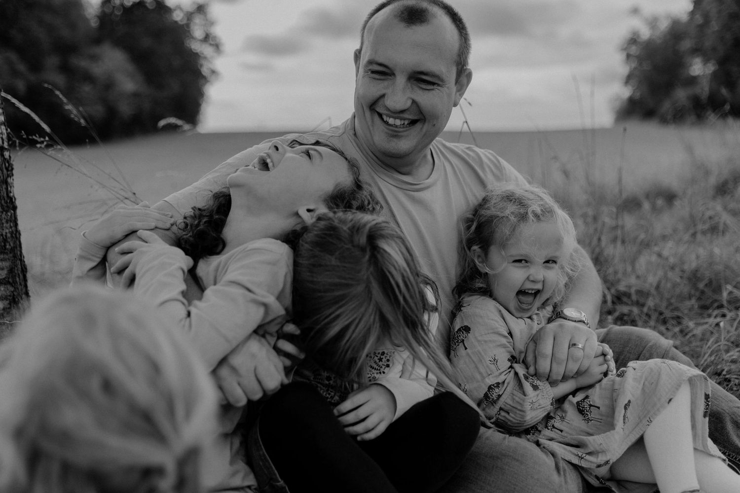 A black and white candid photo of a joyful moment shared between people sitting together in a grassy outdoor setting.