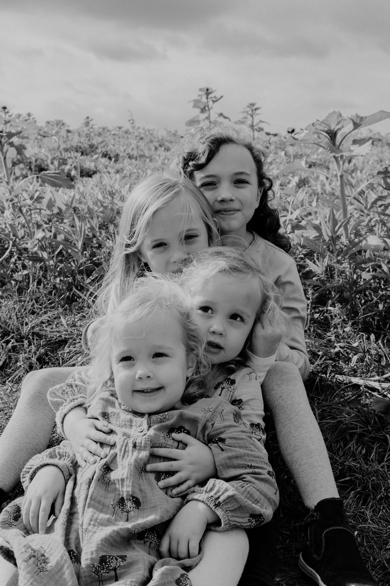 Black and white portrait of a group sitting together among wildflowers in a field on a cloudy day.
