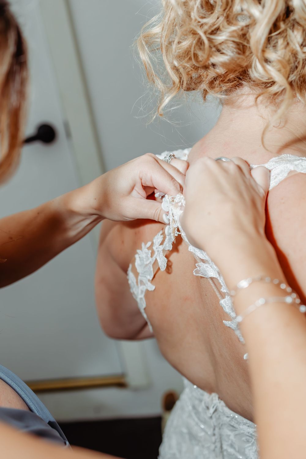 Close-up detail shot of buttoning a delicate lace wedding dress.