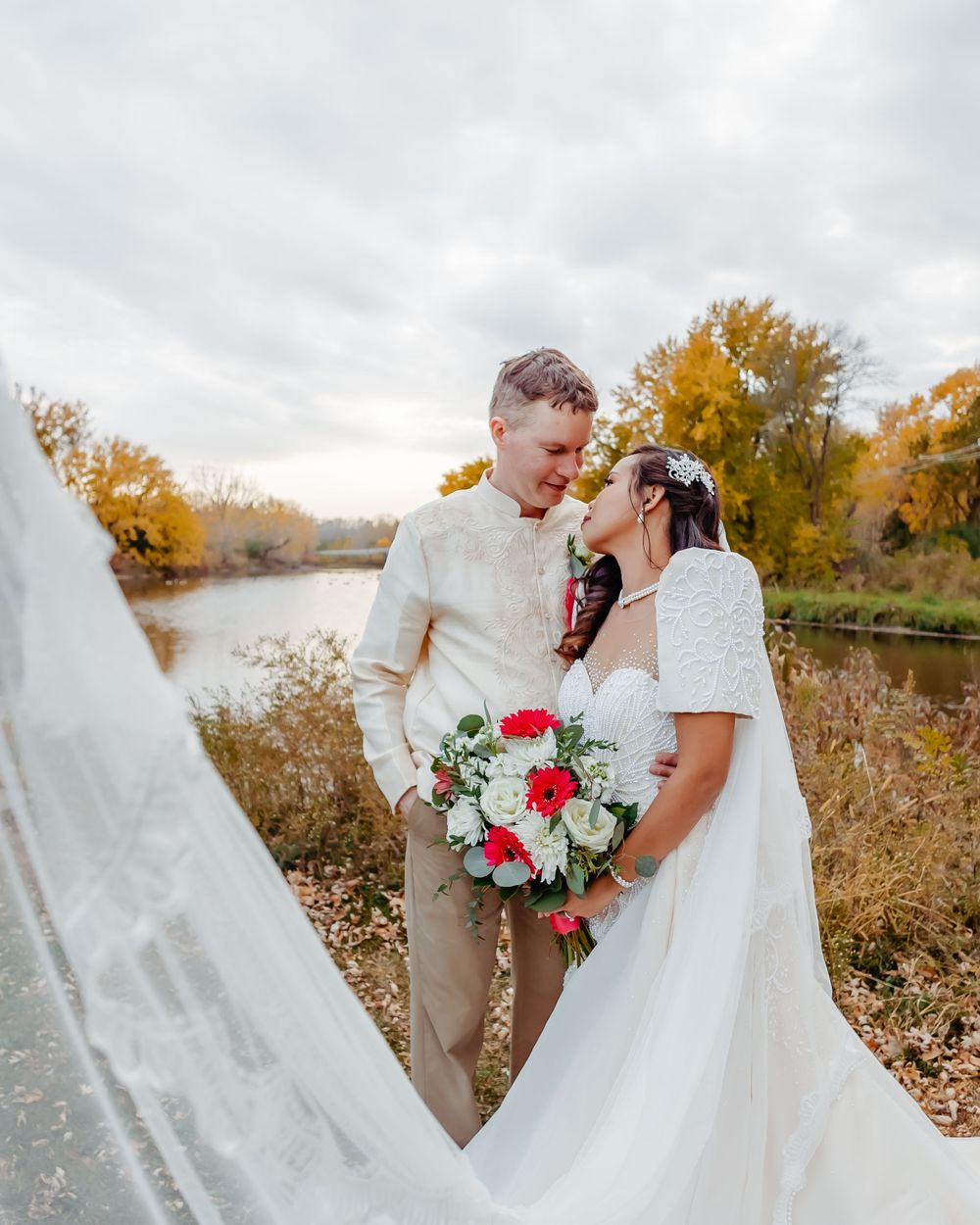 A romantic wedding portrait in a fall setting with flowing white dress and red floral bouquet.
