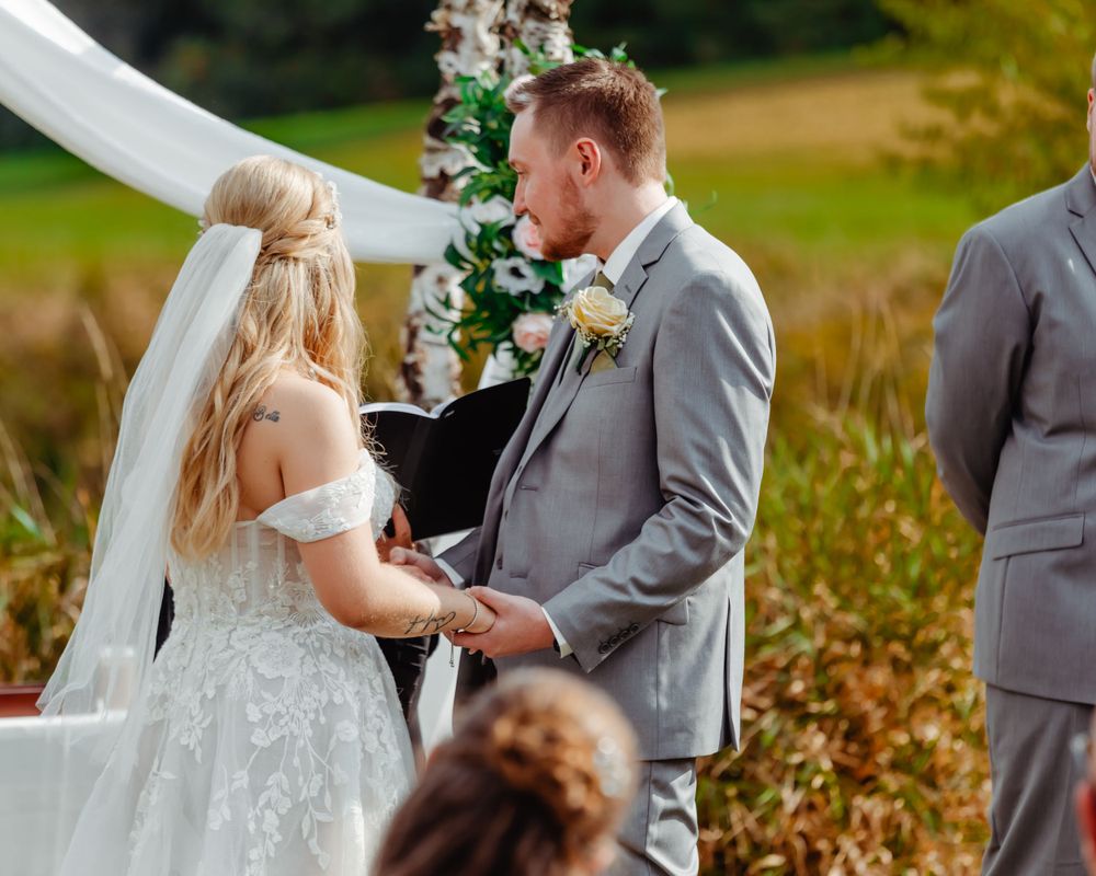Wedding ceremony under white arch with floral decorations and autumn scenery.