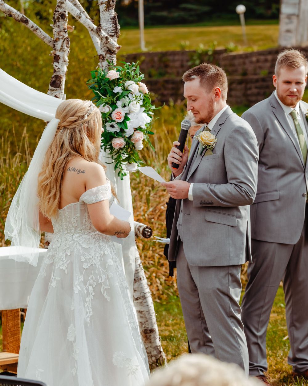 Outdoor wedding ceremony with birch arch and floral arrangements in natural fall setting.
