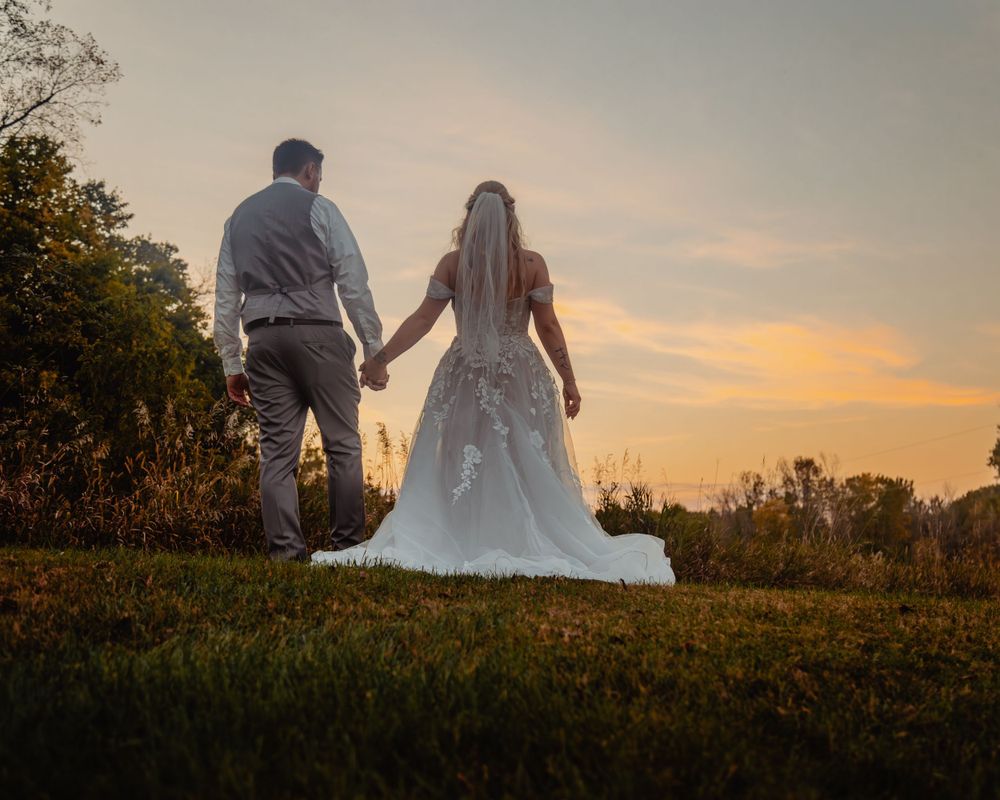 A couple holding hands walks on a hilltop against a golden sunset sky.