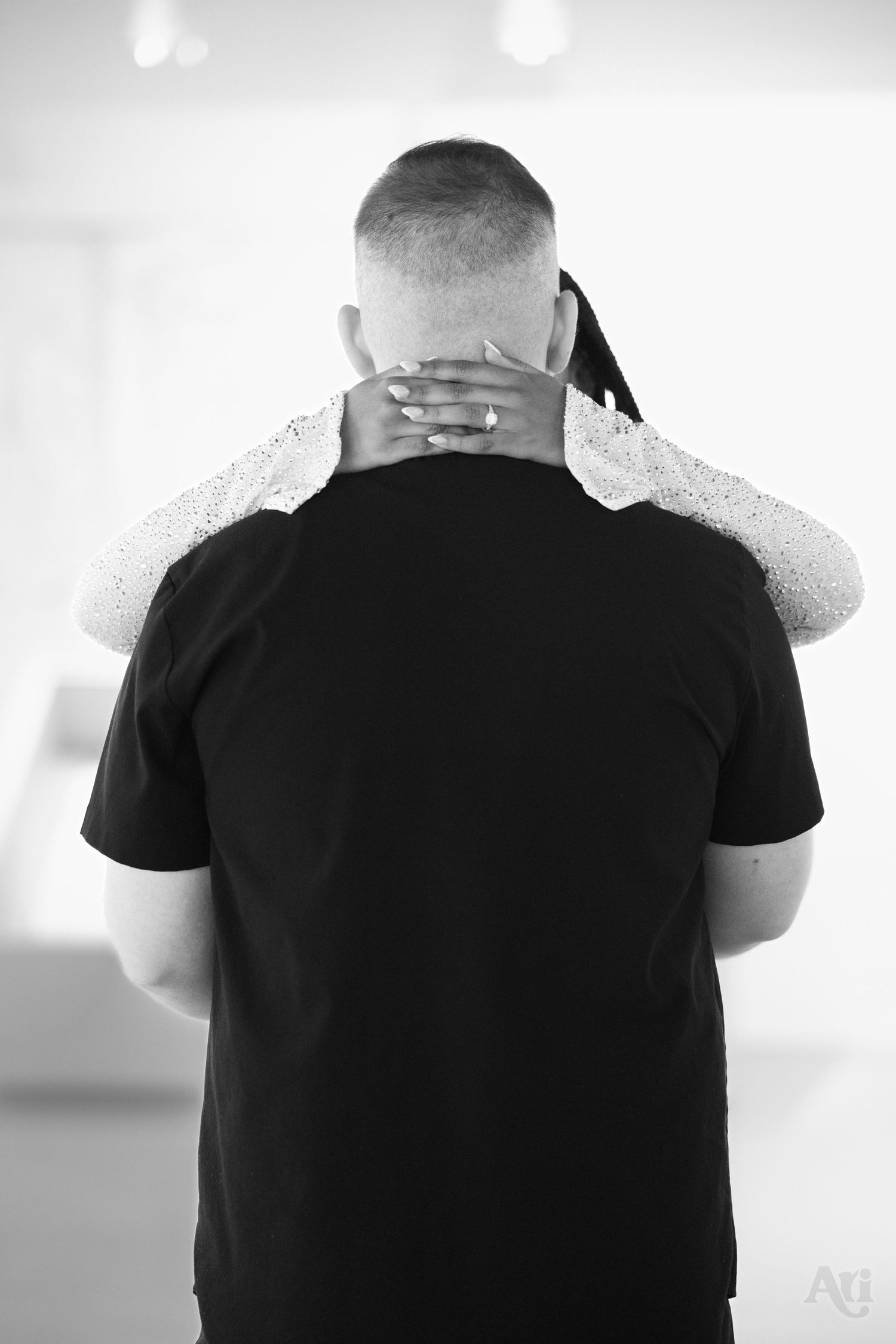 A black and white photo showing hands embracing someone wearing a black t-shirt from behind.