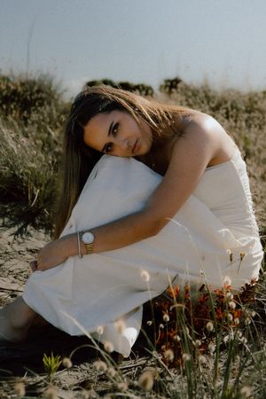 A person in a white dress rests peacefully among wildflowers in a dreamy outdoor setting at golden hour.