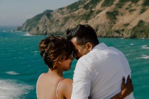 Couple sharing a romantic moment with turquoise ocean and coastal cliffs in the background.