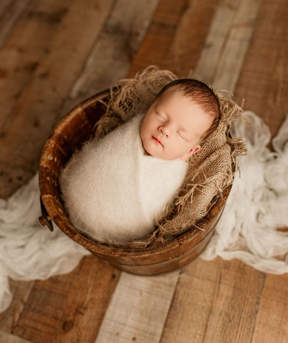 Top view of baby Easton wrapped in cream, resting in a wooden bucket with burlap accents at Bailey's Photography in Southern Ohio.