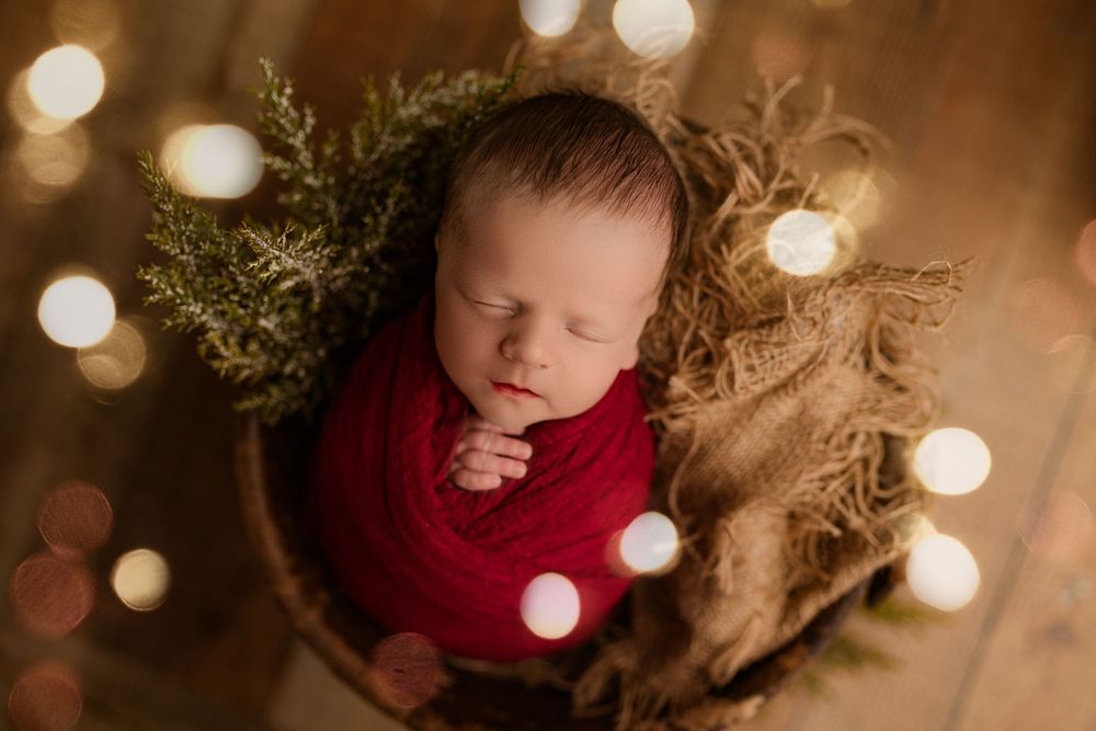 Festive baby Easton in a red wrap with soft lights and greenery, captured in a Christmas setup at Bailey's Photography in Minford, Ohio.