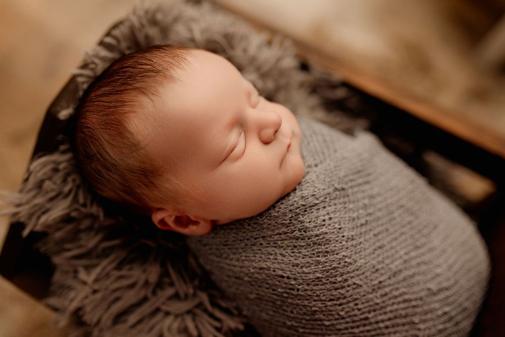 Handsome newborn baby Easton peacefully sleeping, wrapped in soft neutral tones, captured at Bailey’s Photography studio in Minford, Ohio.
