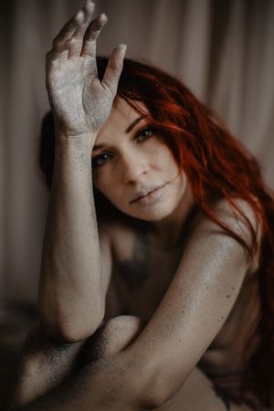 Artistic portrait with raised hand against soft fabric backdrop.