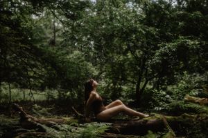 Artistic outdoor portrait on mossy log in lush forest setting.