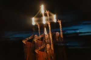 Group in dark robes holds candles aloft during mystical twilight ceremony.