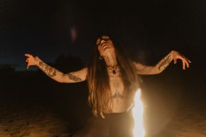 Figure in expressive dance pose illuminated by candlelight against night sky.