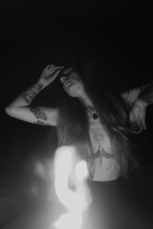 Dramatic black and white portrait with flowing hair and raised arms in ethereal lighting.