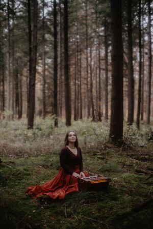 Moody forest photography with pine trees framing figure in red dress with vintage book.