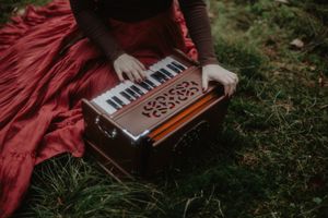 Hands playing harmonium keyboard while wearing flowing red dress outdoors.