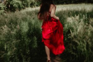 A flowing red dress twirls through tall grass in a romantic outdoor scene.