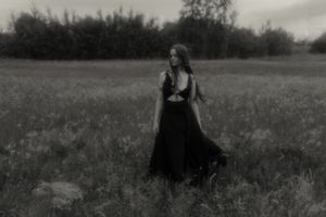 An atmospheric black and white portrait in a windswept field with a flowing dark dress.