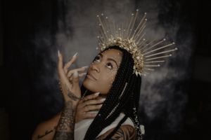 A dramatic portrait with a golden sunburst crown against a dark background.