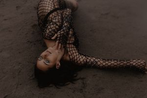 Dramatic overhead shot of a person in fishnet clothing lying on dark ground.