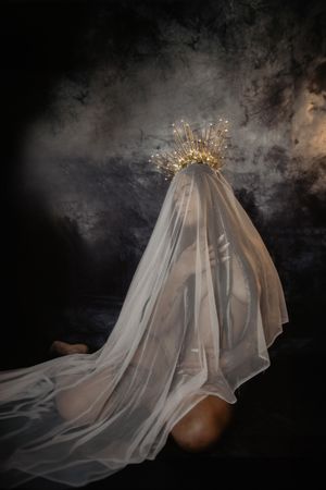 Ethereal figure draped in flowing white veil crowned with golden sunburst headdress.