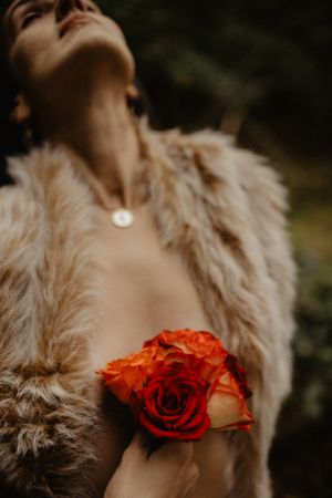 Dramatic close-up with red rose against fur coat in natural lighting.