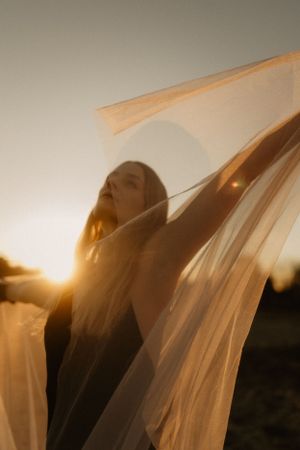 Ätherische Gestalt, in transparenten Stoff gehüllt, vor goldenem Sonnenlicht.