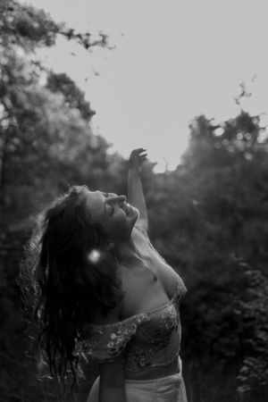 Ethereal portrait in black and white showing upward reaching movement against misty forest backdrop.