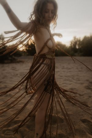 Silhouette dancing on beach at sunset with flowing fringe dress creating motion.