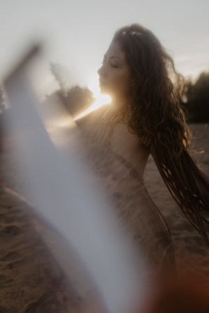 Dreamy backlit portrait with sunburst effect on sandy beach at golden hour.