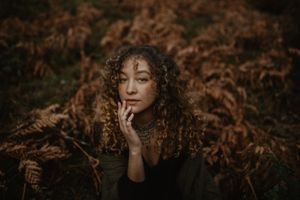 Atmospheric portrait against autumn ferns in warm moody lighting.