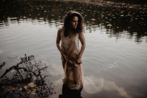 Dreamy portrait by a reflective pond with figure in light flowing dress.