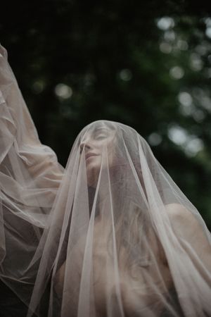 Haunting figure draped in sheer veil creates ethereal atmosphere against dark foliage.