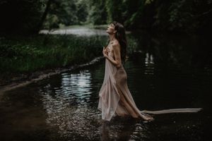 Artistic portrait of figure in flowing dress wading through serene waters at dusk.
