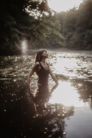 Atmospheric photo captures figure in water with sunlight creating sparkles on the surface.
