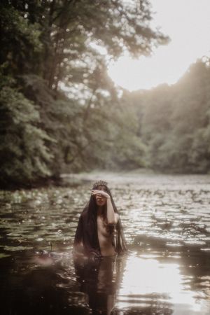 Mystical forest scene with crowned figure emerging from lily-covered water.