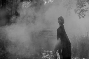 Silhouetted figure stands in misty water during moody foggy photoshoot.