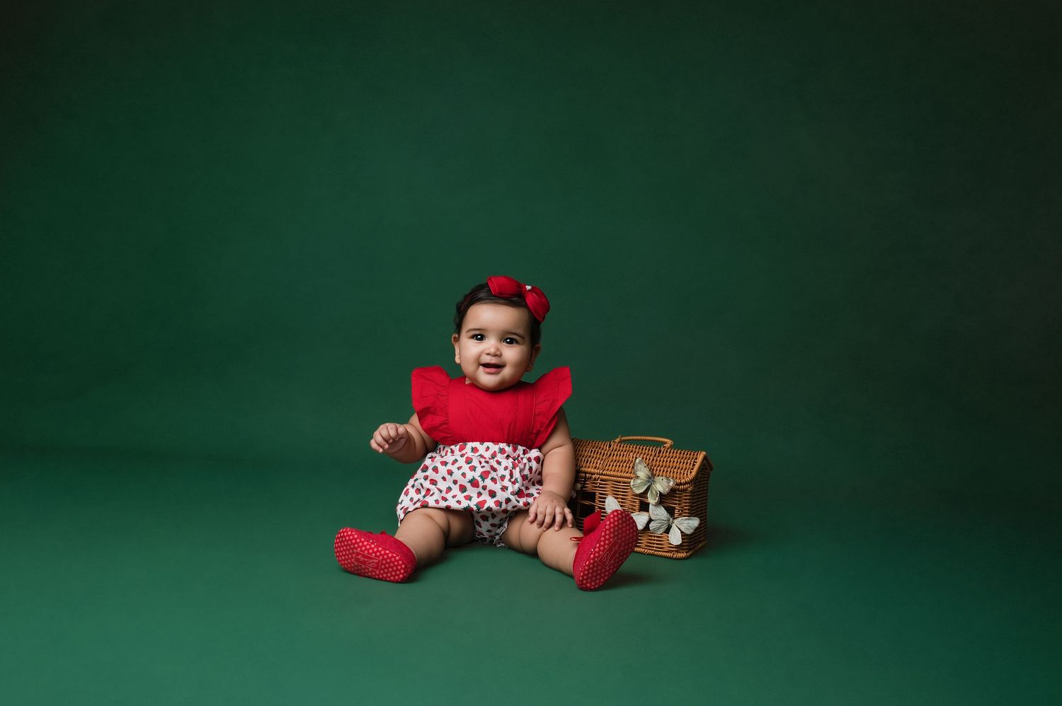 A small baby in a black onesie sits on a white blanket while holding onto the side of a white wooden bed frame.