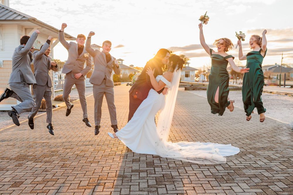 Wedding party jumps in celebration during sunset on a brick patio.