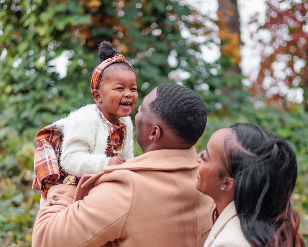 A joyful family moment captured during autumn with colorful fall foliage in the background.