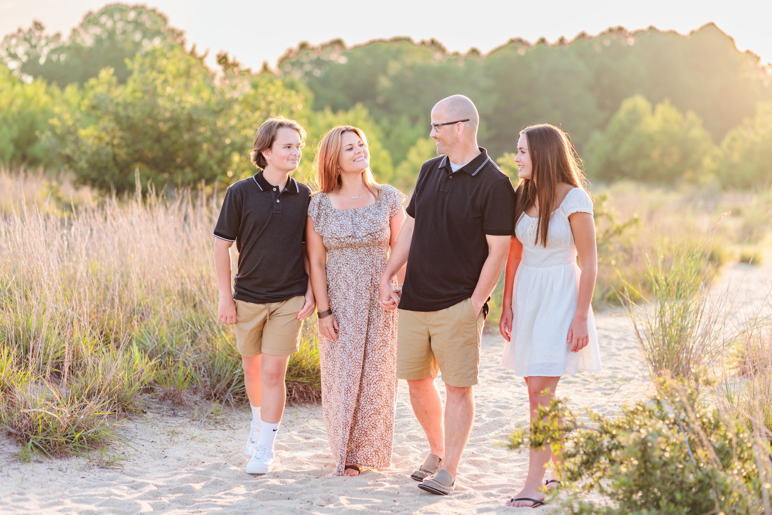 Family portrait in a sunlit field with tall grass and golden evening light.